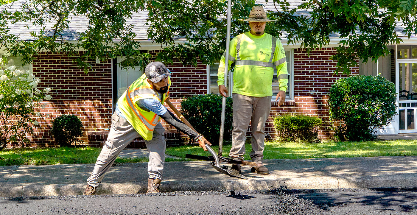 Two men patch a road using shovels. 